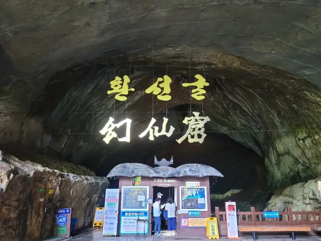 A wide cave mouth in the rock with a ticket booth and visitors at the entrance