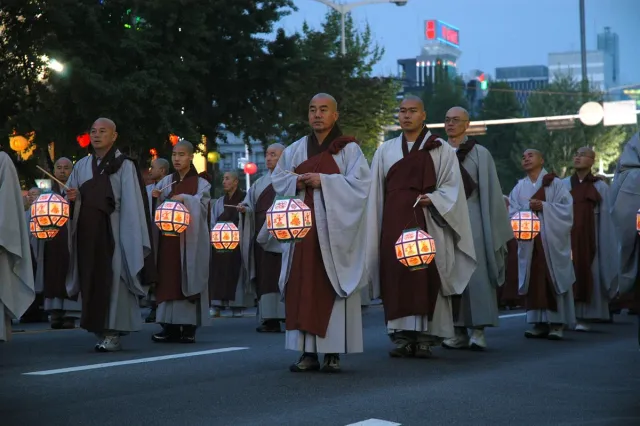 Robed monks walking in procession carrying glowing paper lanterns at dusk