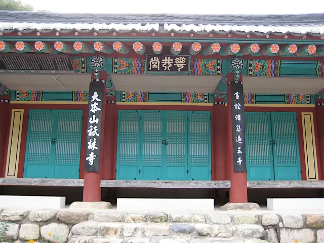 The front of a temple hall with red pillars and beams painted in green and blue