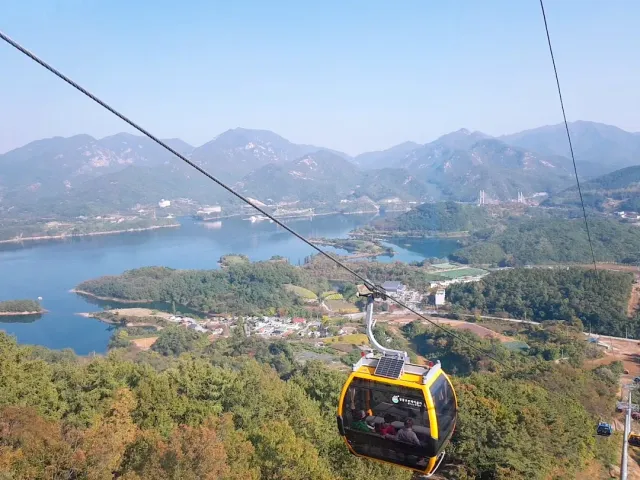 A yellow cable car cabin on a cable, a lake with islands and mountains below it
