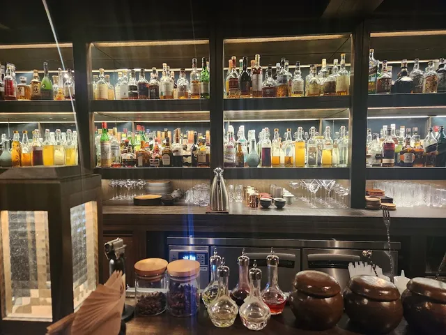 Lit shelves of bottles above a counter, with glass decanters and clay jars in front