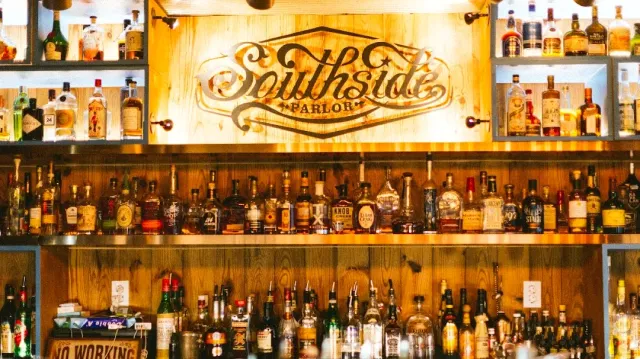 A wooden back bar with a carved sign in the middle and shelves loaded with liquor bottles