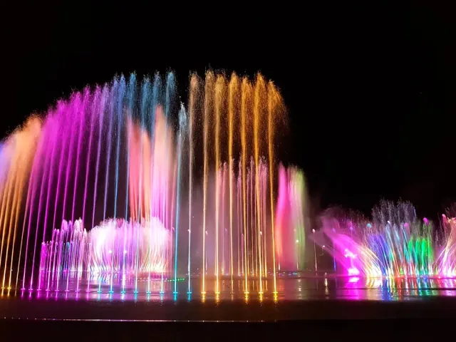 A fountain lit in pink, blue and orange against a black night background