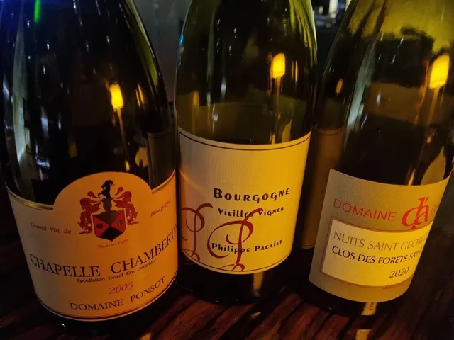 Three bottles of French wine with labels, on a table in warm lighting