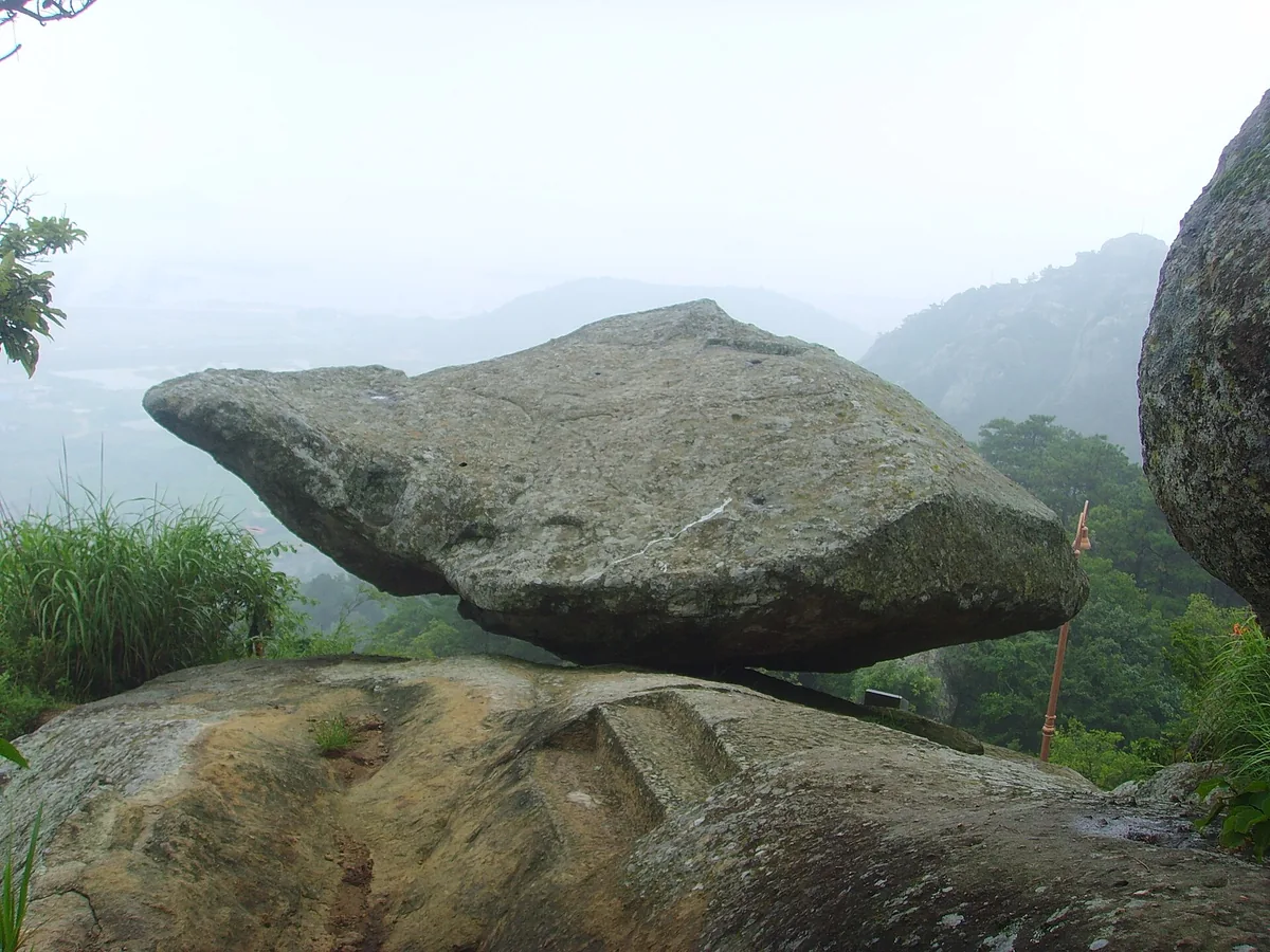 A large balanced boulder on the wooded hillside in light mist