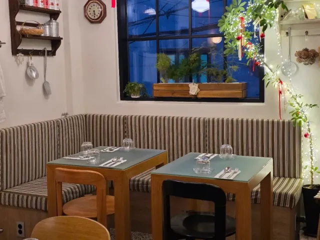 A striped upholstered bench, laid tables and a string of lights beside a dark window