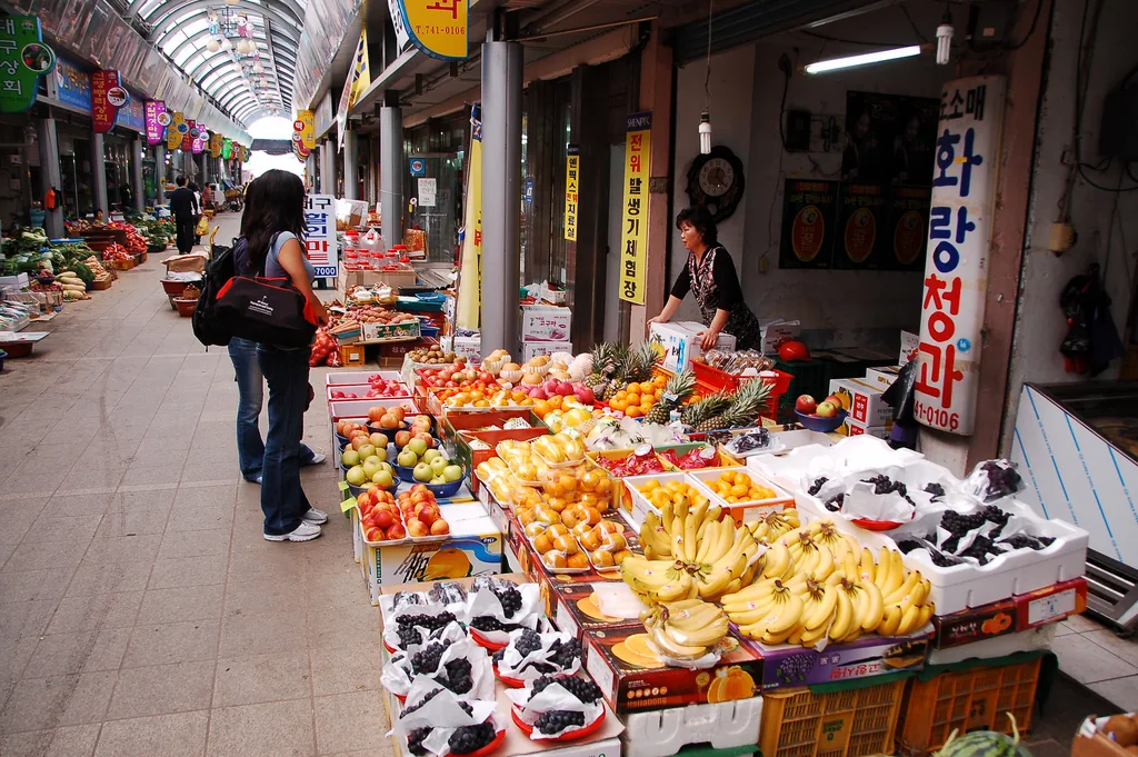 A colourful fruit stall along a covered market aisle, with Korean signs above
