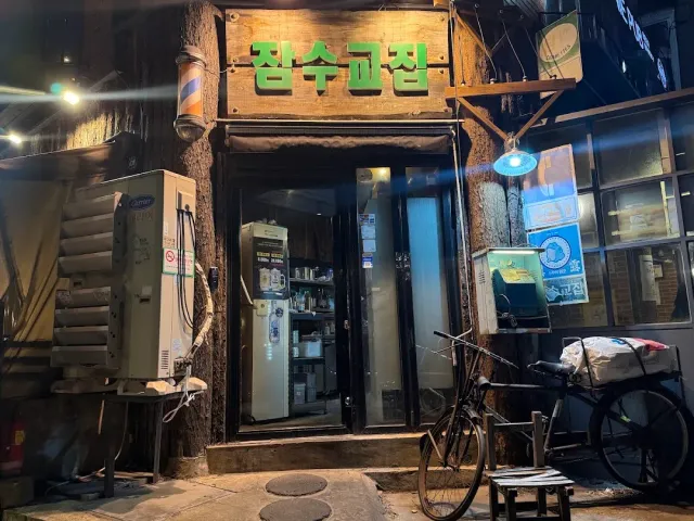 A small shopfront in an alley at night, a bicycle, a stool and a lit wooden sign