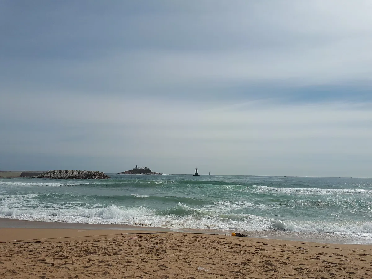 The sand and waves at Sokcho Beach, with the breakwater behind