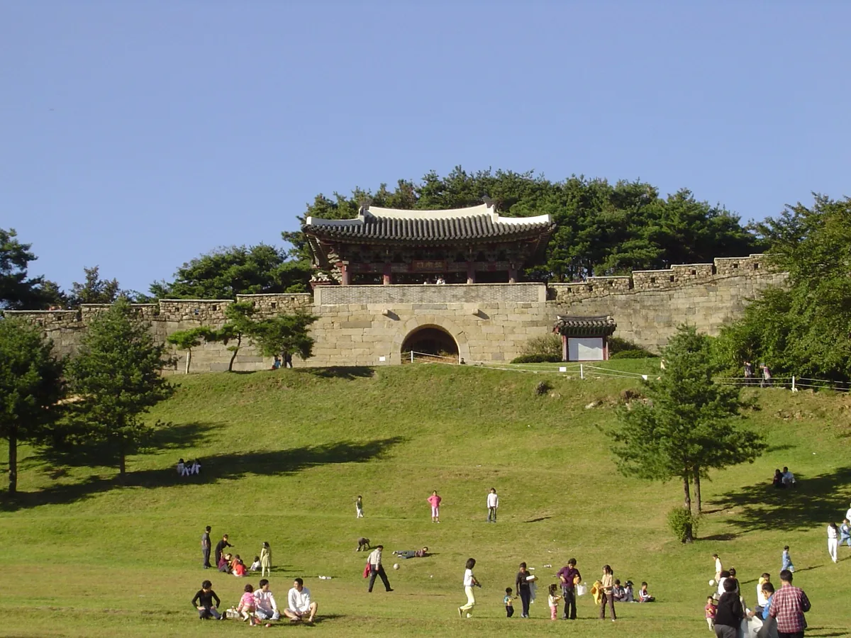 The gate of Sangdangsanseong Fortress in Cheongju, above the grassy slope with visitors on it