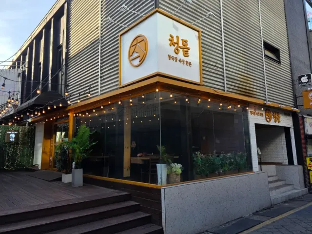 A corner building at dusk with a golden sign, strings of bulbs and a glass front