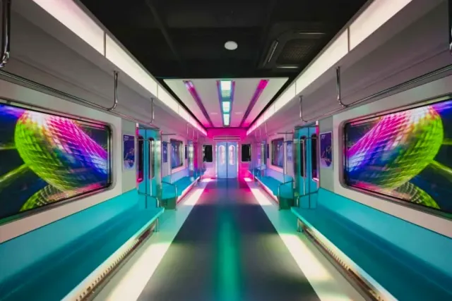 The inside of a train car with colorful screens in the walls and pink and green lighting