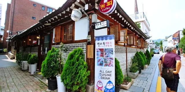 A traditional house along an alley with a tiled roof, a round sign and shrubs in pots