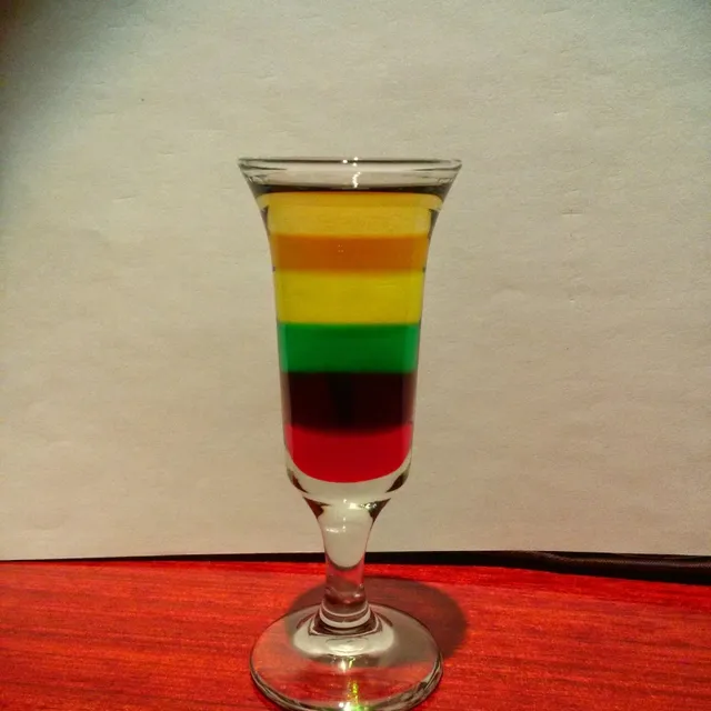 A narrow shot glass with layers of drink in red, green, yellow and orange