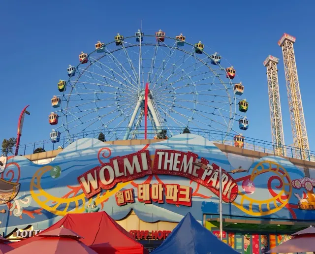 A colorful ferris wheel above a painted amusement park gate under a blue sky