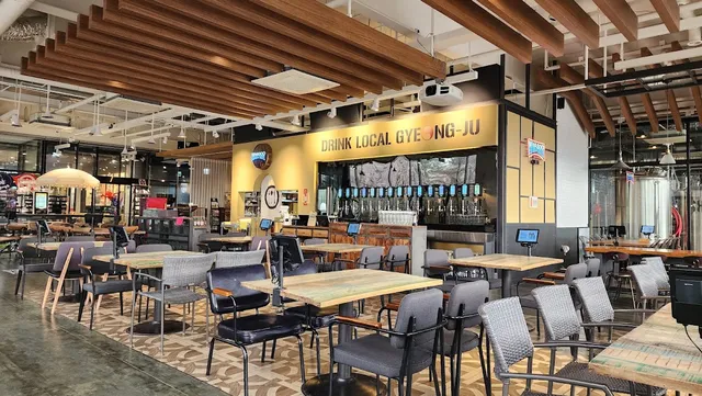A wide hall with wooden tables, a beamed ceiling and a long counter of beer taps