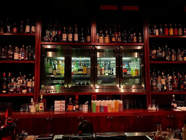A red wooden wall packed with bottles, with lit chilled cabinets above the counter