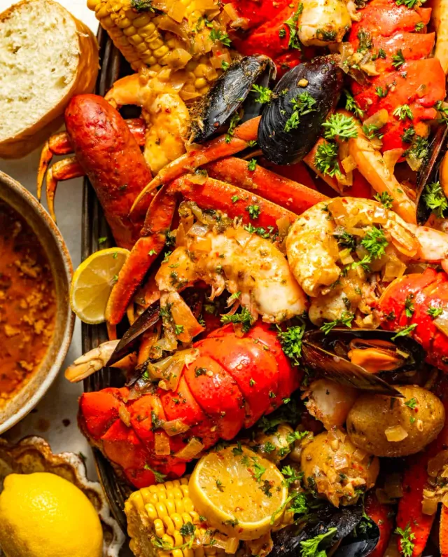 A seasoned seafood tray with a lobster tail, crab legs, shrimp, corn and lemon
