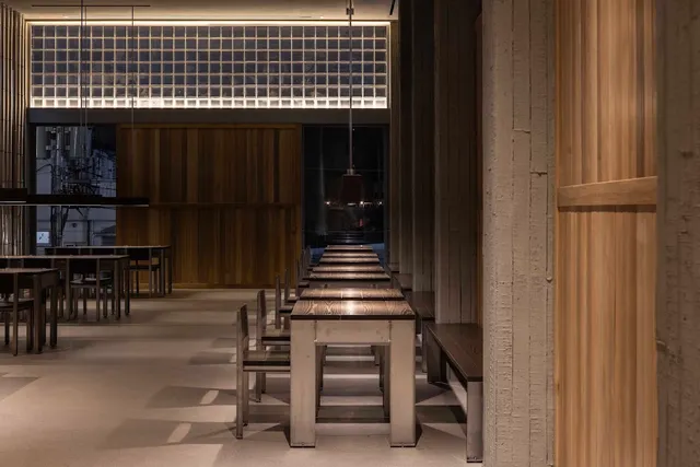 A hall with long wooden tables and benches, wooden walls and a lit glass block ceiling