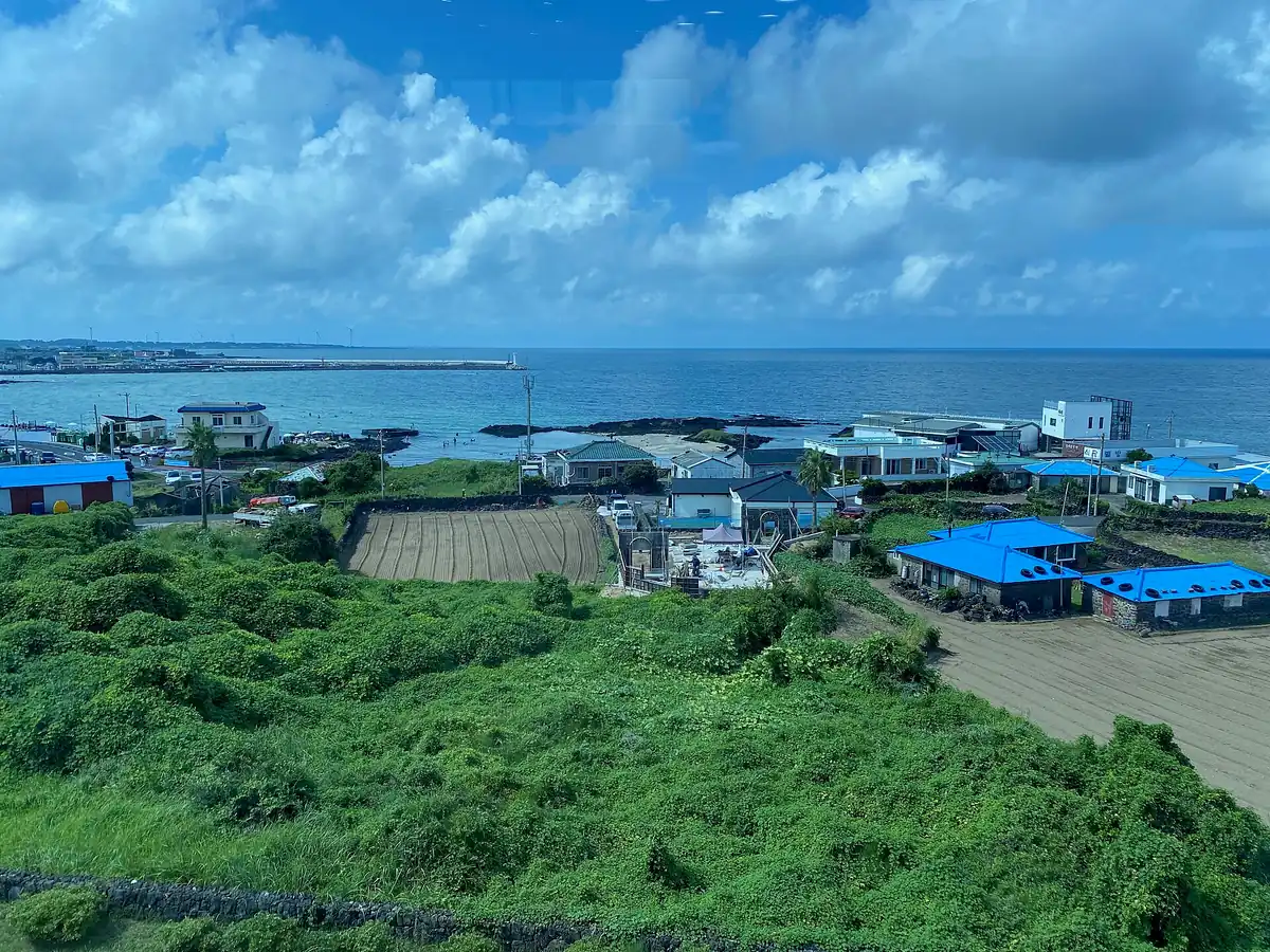 Coastal village of blue roofed houses and ploughed fields on a green slope above a blue sea