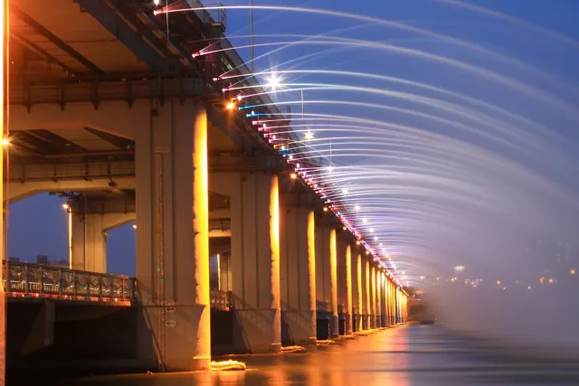 Lit jets of water spilling along the length of a bridge at night