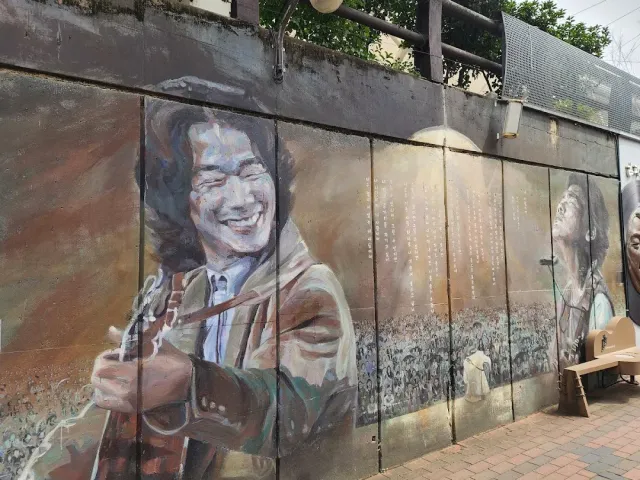A wall painting of a smiling man with a guitar on a long concrete wall