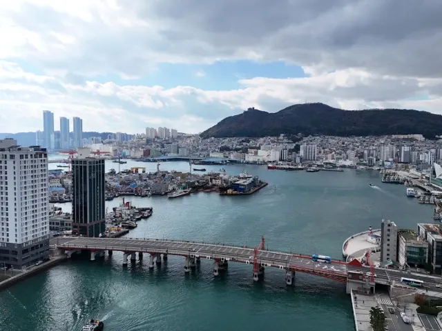 An urban harbor from a high vantage with a low bridge crossing a channel and a green ridge behind