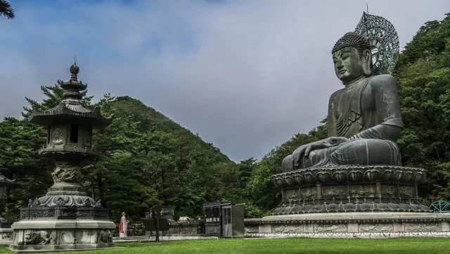 A huge seated bronze Buddha on a stone platform surrounded by trees