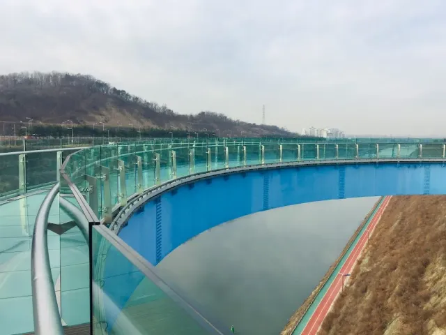 A glass railing along the edge of a curving blue bridge above a water canal