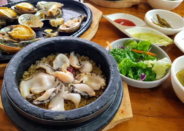 A stone pot of rice with abalone slices, and behind it a pan of grilled abalone in the shell