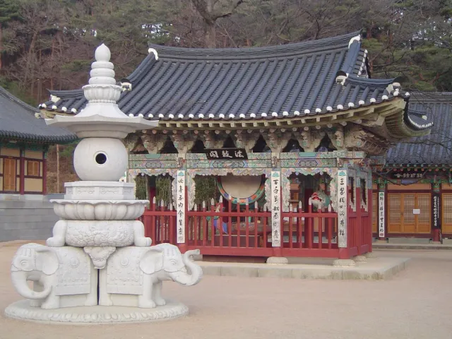 A white stone pillar on carved elephants in front of a painted temple hall
