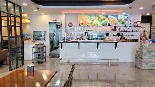 An interior with a white tiled counter, an open kitchen behind and photos of dishes on the wall