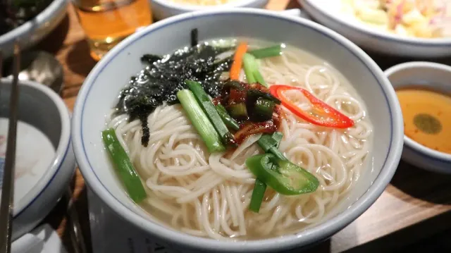 A bowl of thin noodles in clear broth with seaweed, spring onion and red pepper