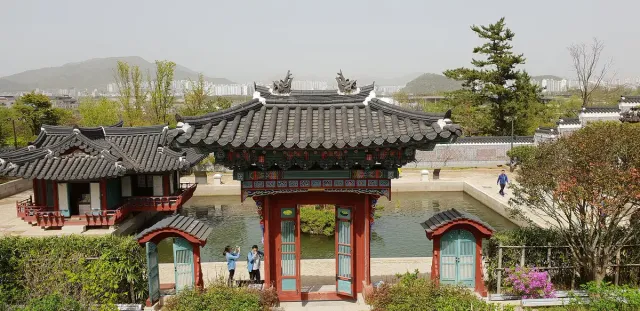 A traditional wooden pavilion and red bridge over a pond in a landscaped garden