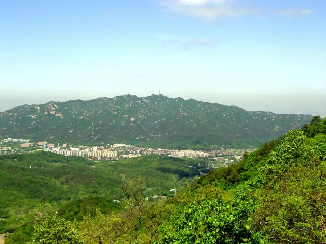 A green forested mountain ridge stretching above the city in light haze