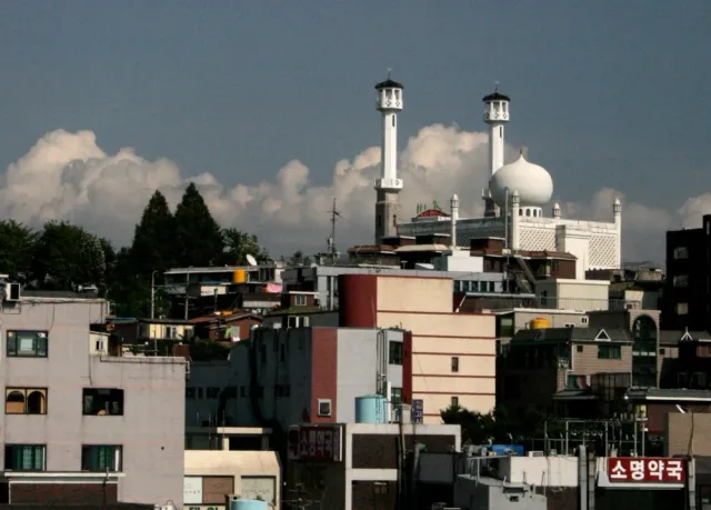 A mosque with a white dome and two minarets above a dense neighbourhood of rooftops