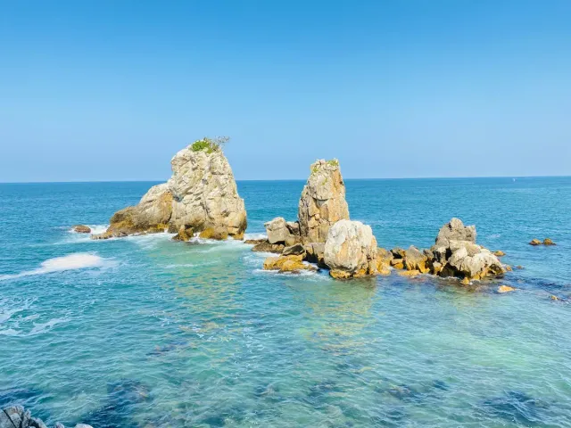 Two tall rocks standing in clear turquoise water close to the shoreline