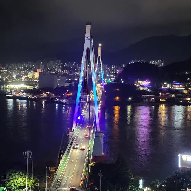 A cable-stayed bridge lit in blue over a bay, with the city lights and hills behind at night
