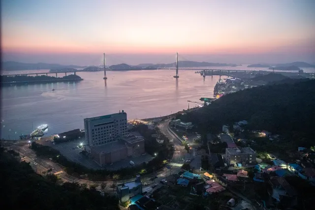 A wide bay with a long suspension bridge and city lights at sunset