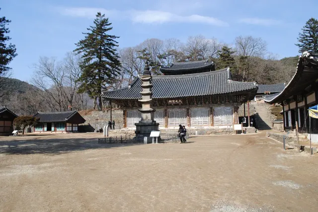 A stone pagoda in a broad temple courtyard ringed by wooden halls and hills