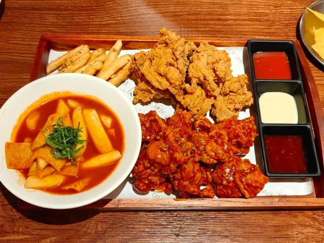 A tray with fried chicken, rice cakes in red sauce and three dips