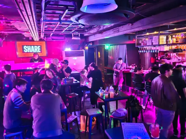 A basement bar in pink neon light, a dense crowd around high tables and a lit sign