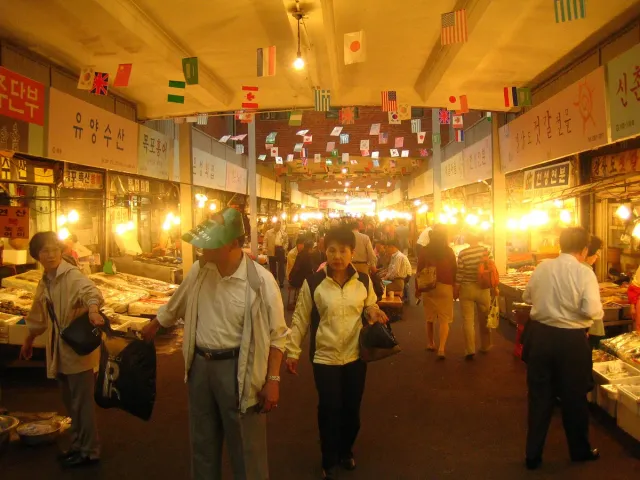 A brightly lit alley of food stalls with crowded tables and diners