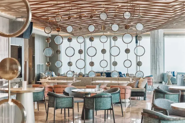 A spacious lounge with turquoise armchairs and strings of metal circles hanging from the ceiling