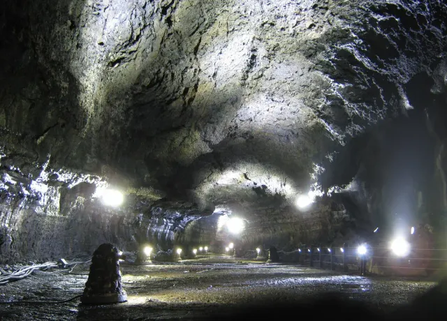 A wide dark lava tunnel with floor lighting along the walkway
