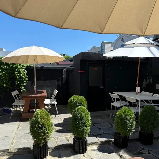 A paved courtyard with pale parasols, white tables and pots of trimmed shrubs