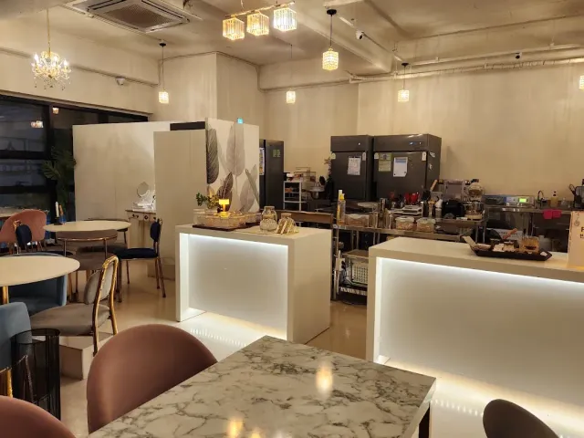 A space with marble tables, pink chairs, small chandeliers and a lit counter