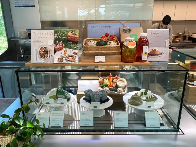 A display case of green tinted cakes on white stands, product posters behind