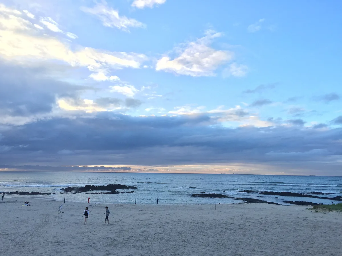 Shallow clear water at a beach on Jeju, a few people wading and a wide sky