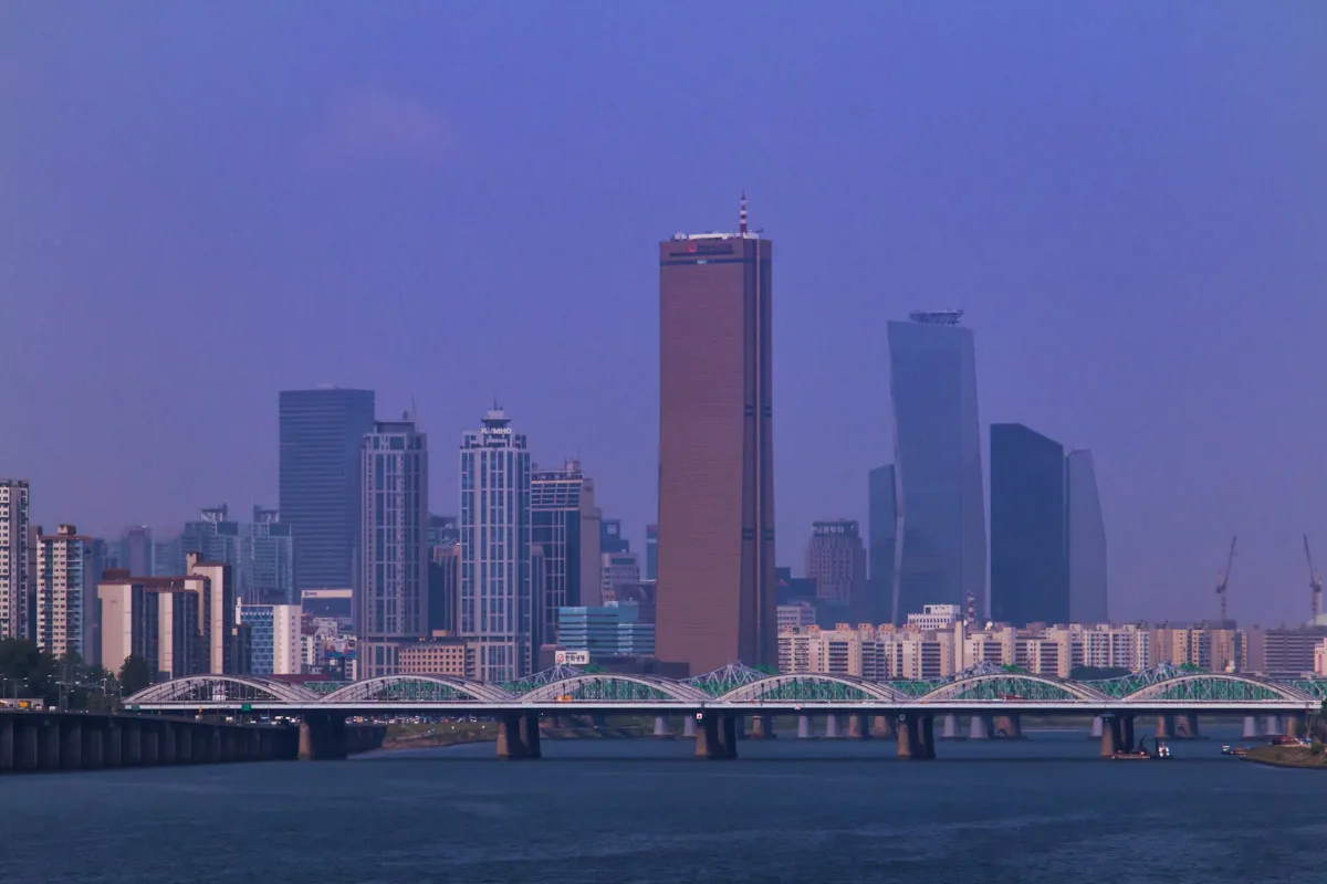 A tall bronze coloured tower at the centre of a riverside skyline, with an arched bridge in front